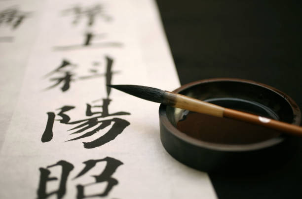 Artiste en kimono noir et blanc peignant sur toile blanche, pinceaux et fleurs roses sur table.